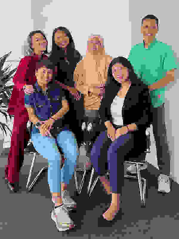 Gruppe von sechs Personen in einem modernen Büro, posierend für ein Foto. Sie stehen und sitzen zusammen, umgeben von einem Pflanzenarrangement.