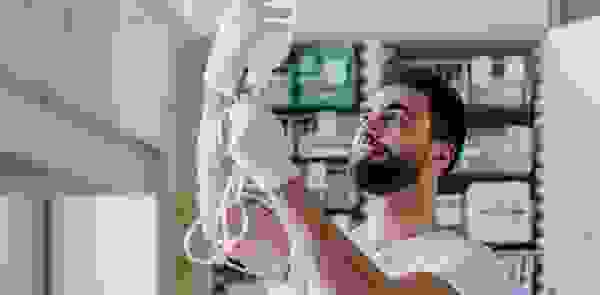 Ein Gesundheitspersonal hält eine Infusionsflasche in der Hand und schaut aufmerksam darauf. Im Hintergrund sind Medikamente und medizinische Ausrüstung sichtbar.