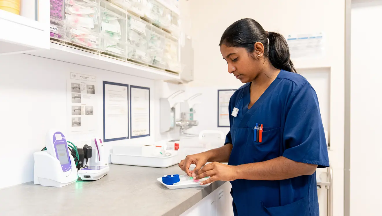 Eine Krankenschwester in blauer Uniform bereitet Materialien auf einer Arbeitsplatte in einem medizinischen Umfeld vor.