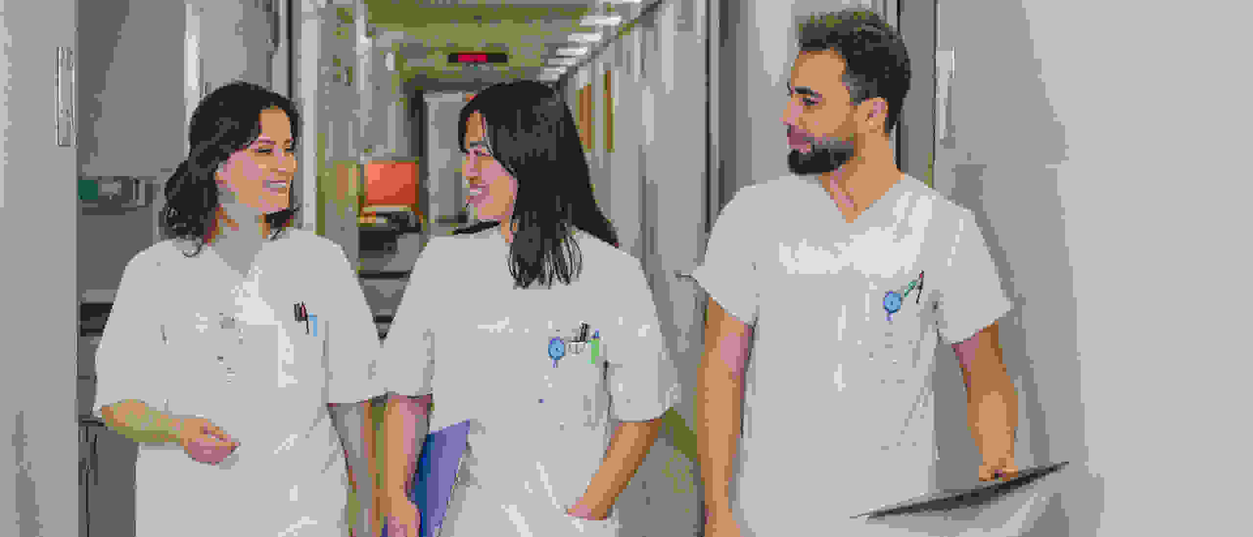 Drei medizinische Fachkräfte in weißen Arbeitskleidungen, die lächelnd einen Flur im Krankenhaus entlanggehen, dabei Notizen und Dokumente halten.