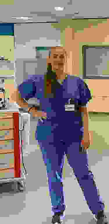 Frau in blauer medizinischer Kleidung posiert für eine Kamera in einem Krankenhaus.