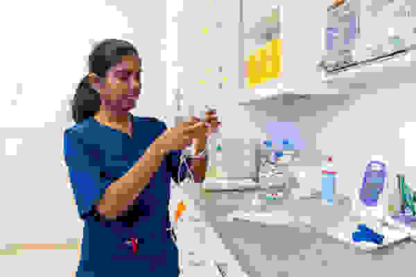 Eine Fachkraft in blauer Dienstkleidung arbeitet an medizinischen Geräten und Zubehör in einem klinischen Umfeld.