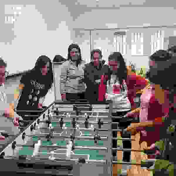 Eine Gruppe von Frauen spielt Tischfußball in einem hellen Raum. Sie sind konzentriert und haben Spaß.