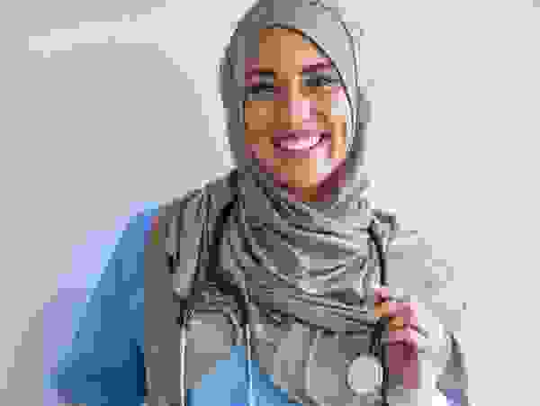 Eine lächelnde medizinische Fachkraft in blauer Kleidung und einem Hijab, die ein Stethoskop hält.