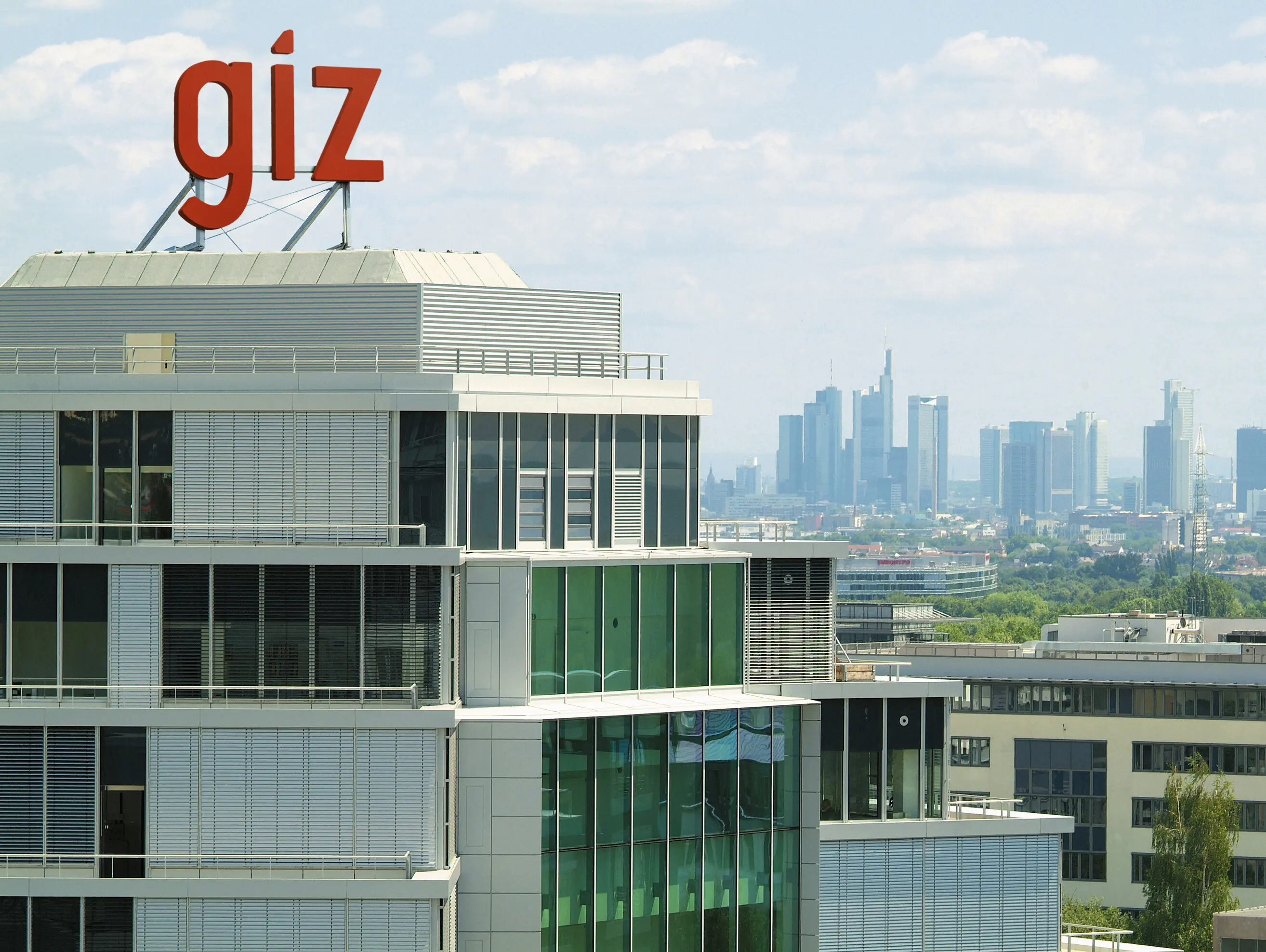 Ein modernes Bürogebäude mit dem roten Schriftzug "giz" auf dem Dach und im Hintergrund die Skyline einer Stadt.