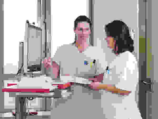 Zwei Krankenschwestern in weißen Kitteln besprechen Patientendaten an einem Computerarbeitsplatz in einem modernen Krankenhaus.