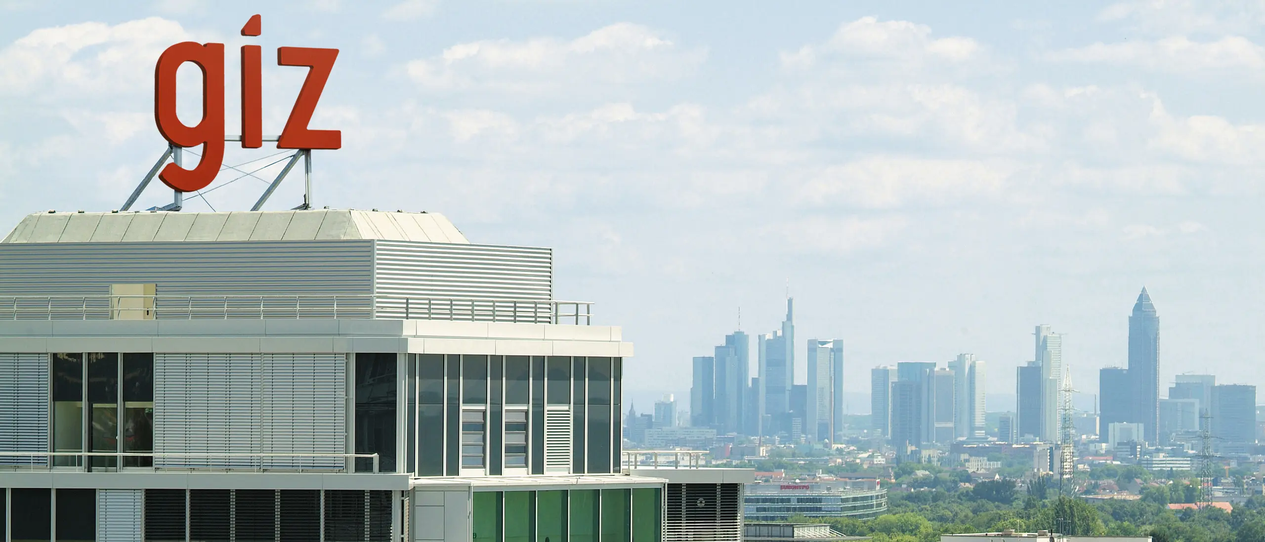 A modern office building with the red lettering &ldquo;giz&rdquo; on the roof and the skyline of a city in the background.
