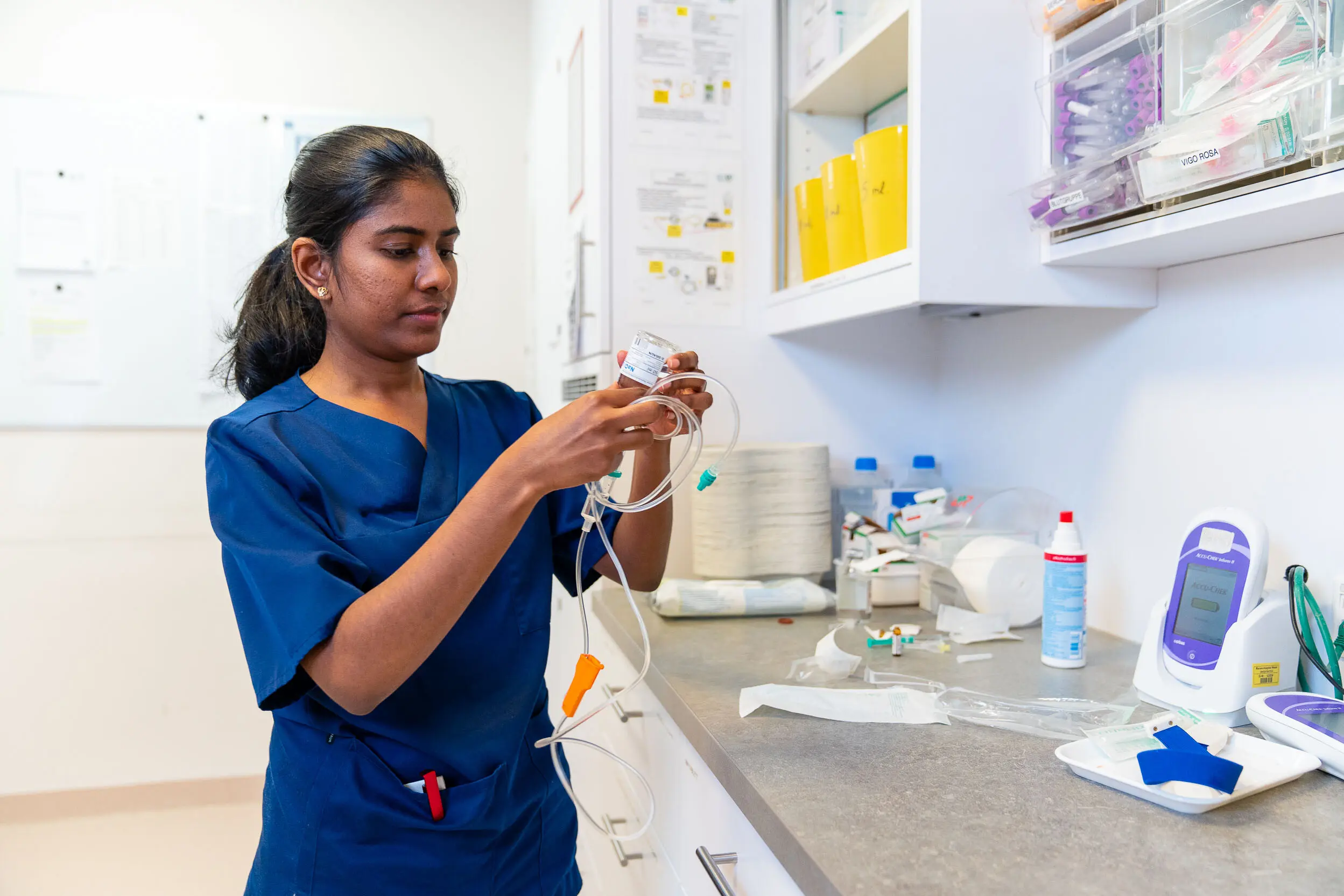 A specialist in blue uniforms works on medical equipment and accessories in a clinical environment.