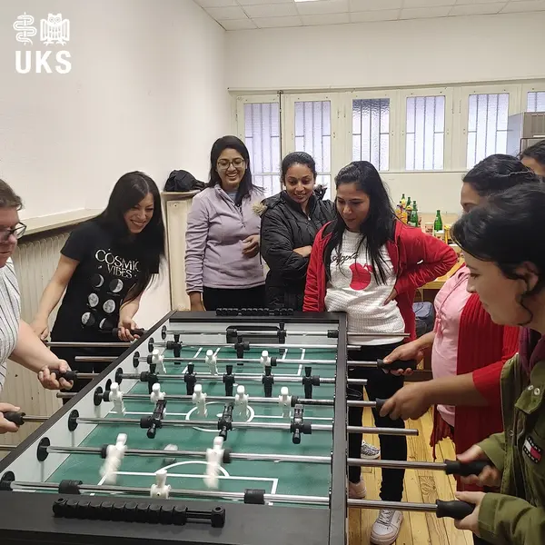 A group of women are playing table soccer in a bright room. They are focused and having fun.