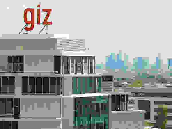 A modern office building with the red lettering “giz” on the roof and the skyline of a city in the background.