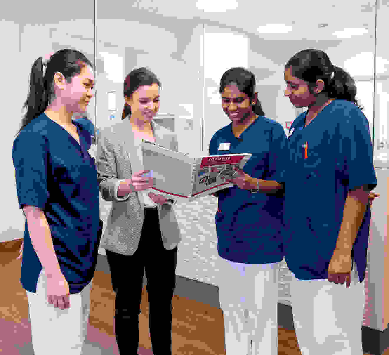 Dans un environnement médical moderne, quatre personnes consultent ensemble un livre. Trois d'entre elles portent des vêtements de travail bleus, tandis qu'une personne est vêtue d'un blazer gris.