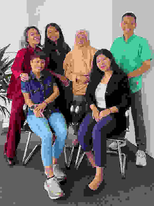 Group of six people in a modern office, posing for a photo. They stand and sit together, surrounded by an arrangement of plants.