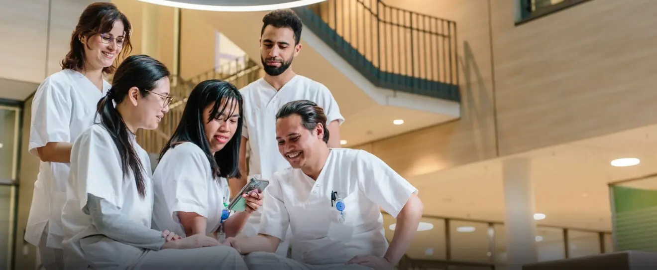 Groupe de professionnels de la santé souriant et regardant un téléphone dans un espace moderne.