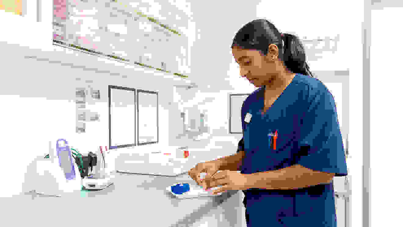 A nurse in a blue uniform prepares materials on a worktop in a medical environment.