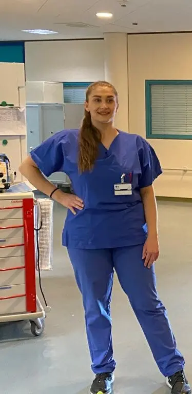 Femme en tenue médicale bleue posant pour un appareil photo dans un hôpital.
