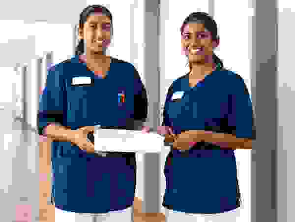 Two nurses in blue uniforms stand in the hospital corridor holding a white box.