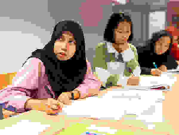 Un groupe de jeunes femmes assises à une table, concentrées sur leurs notes et leur écriture pendant qu'elles participent à un cours.