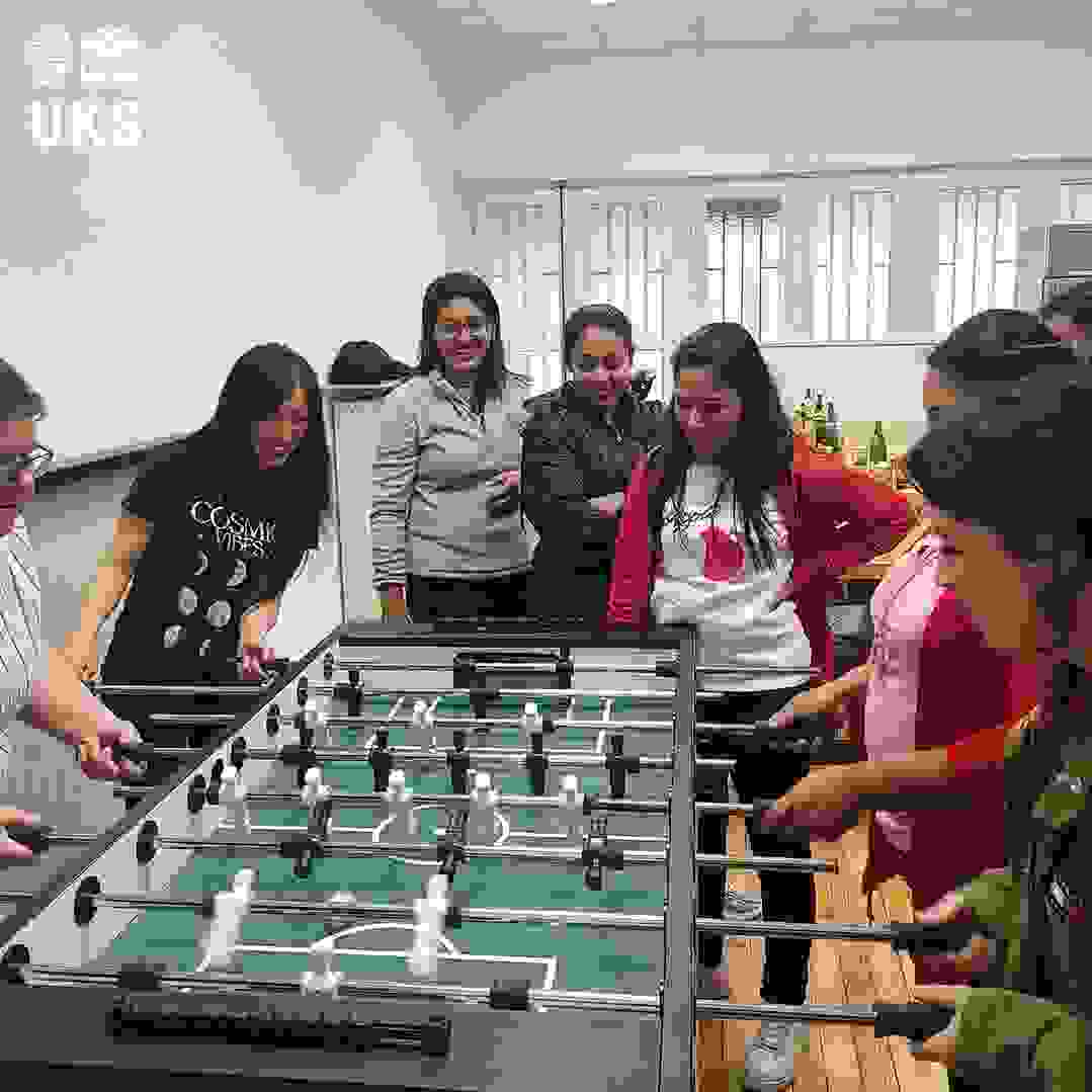Sekelompok wanita sedang bermain sepak bola meja di sebuah ruangan yang terang. Mereka fokus dan bersenang-senang.