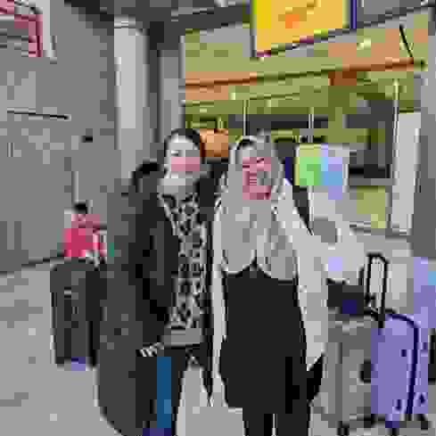 Dua wanita yang tersenyum berdiri di sebuah ruang resepsi, dikelilingi oleh koper-koper.