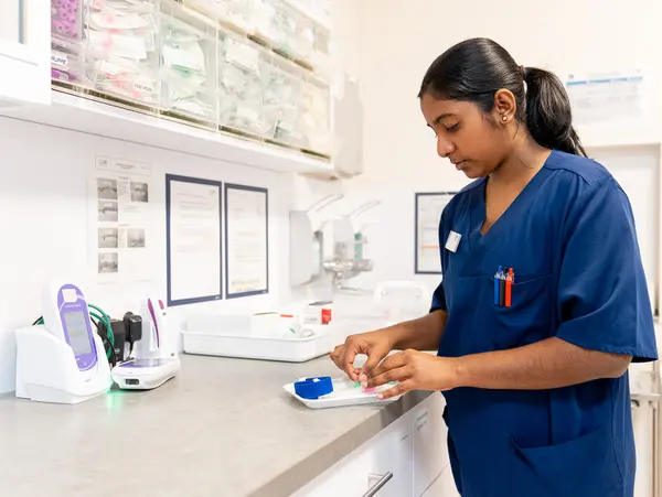 A nurse in a blue uniform prepares materials on a worktop in a medical environment.